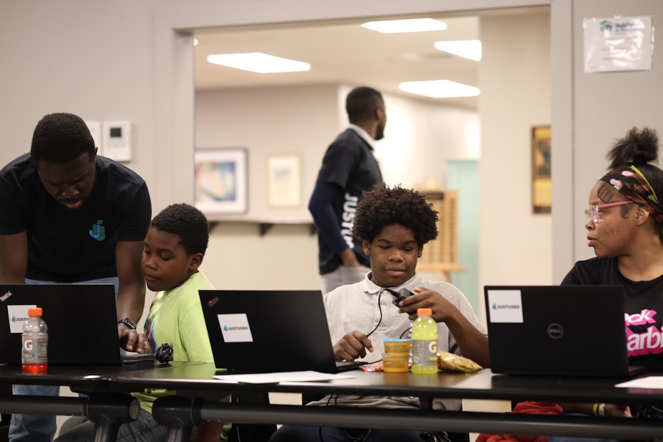 Young people working at laptops around a long table, with team members alongside them.