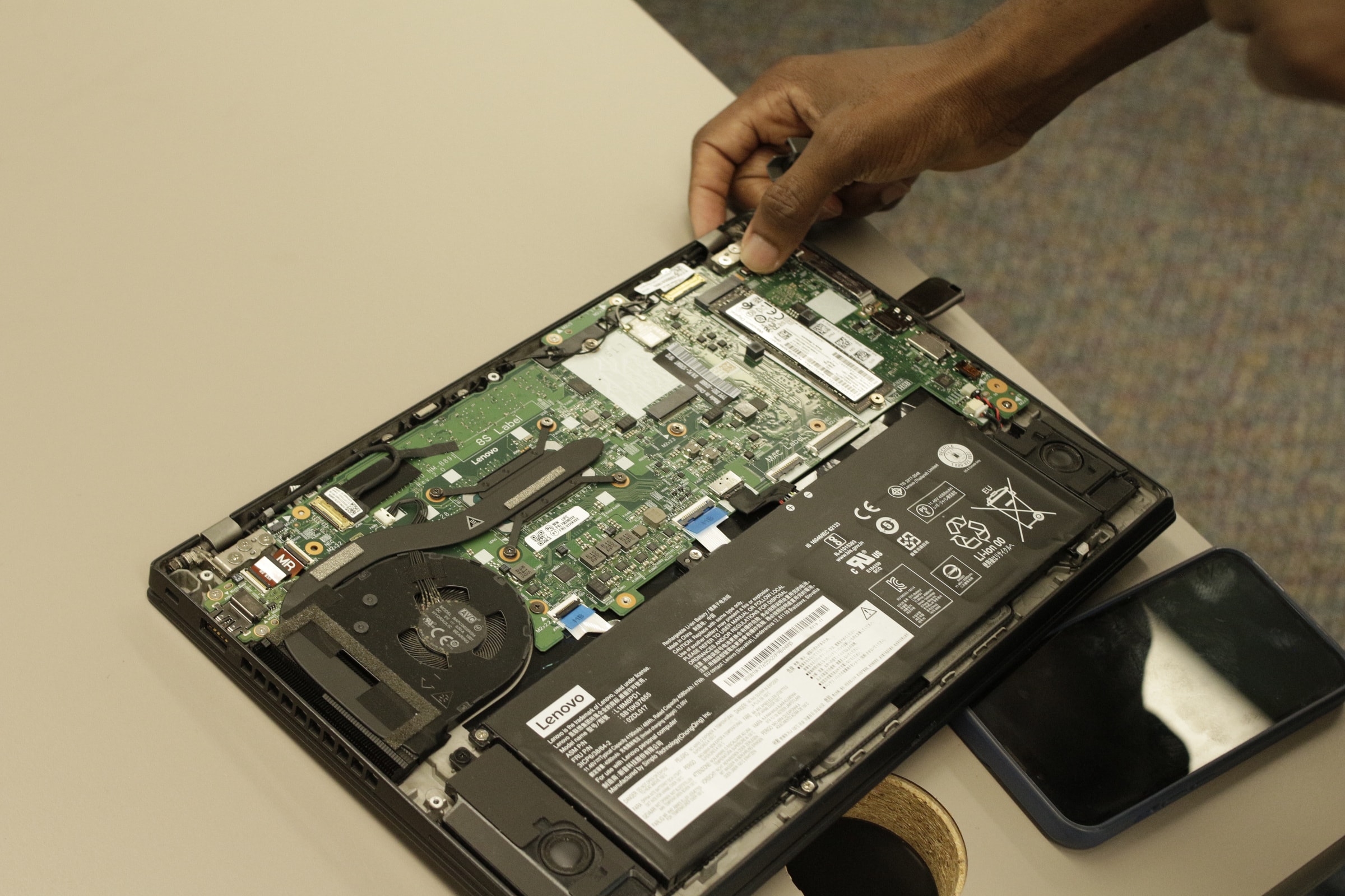 Close-up of an opened laptop with its back panel removed, hands working on the internals.