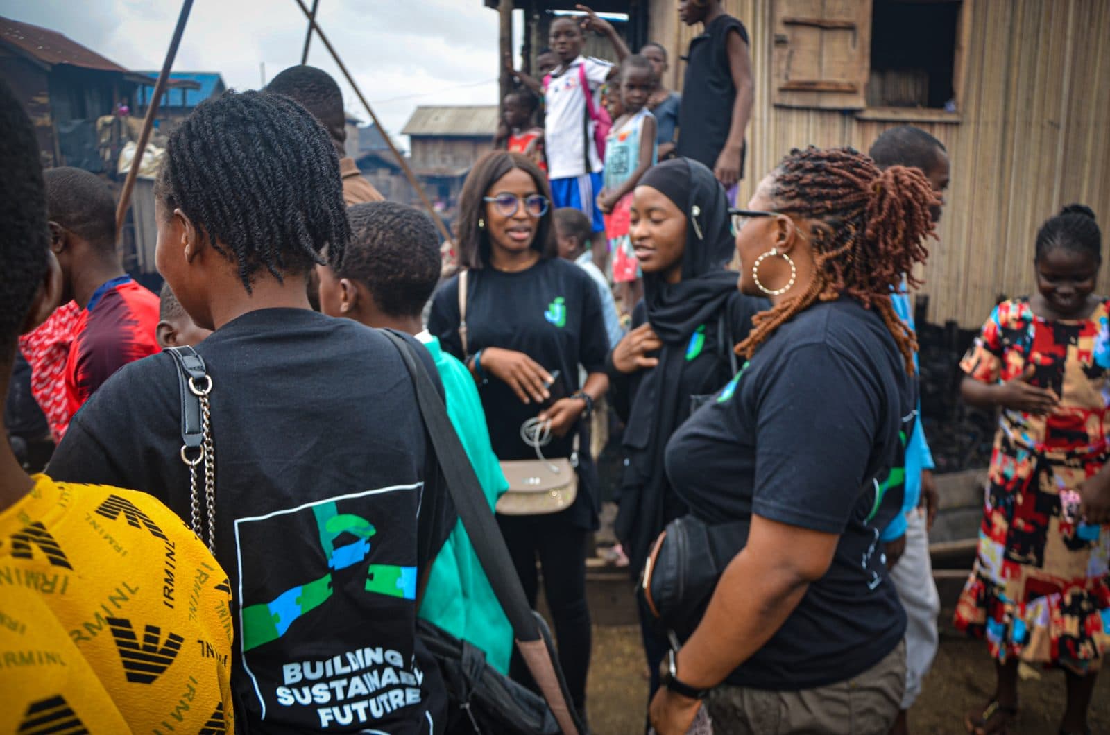 Team members in JustUsedTech shirts talking with residents in a Lagos waterfront community.