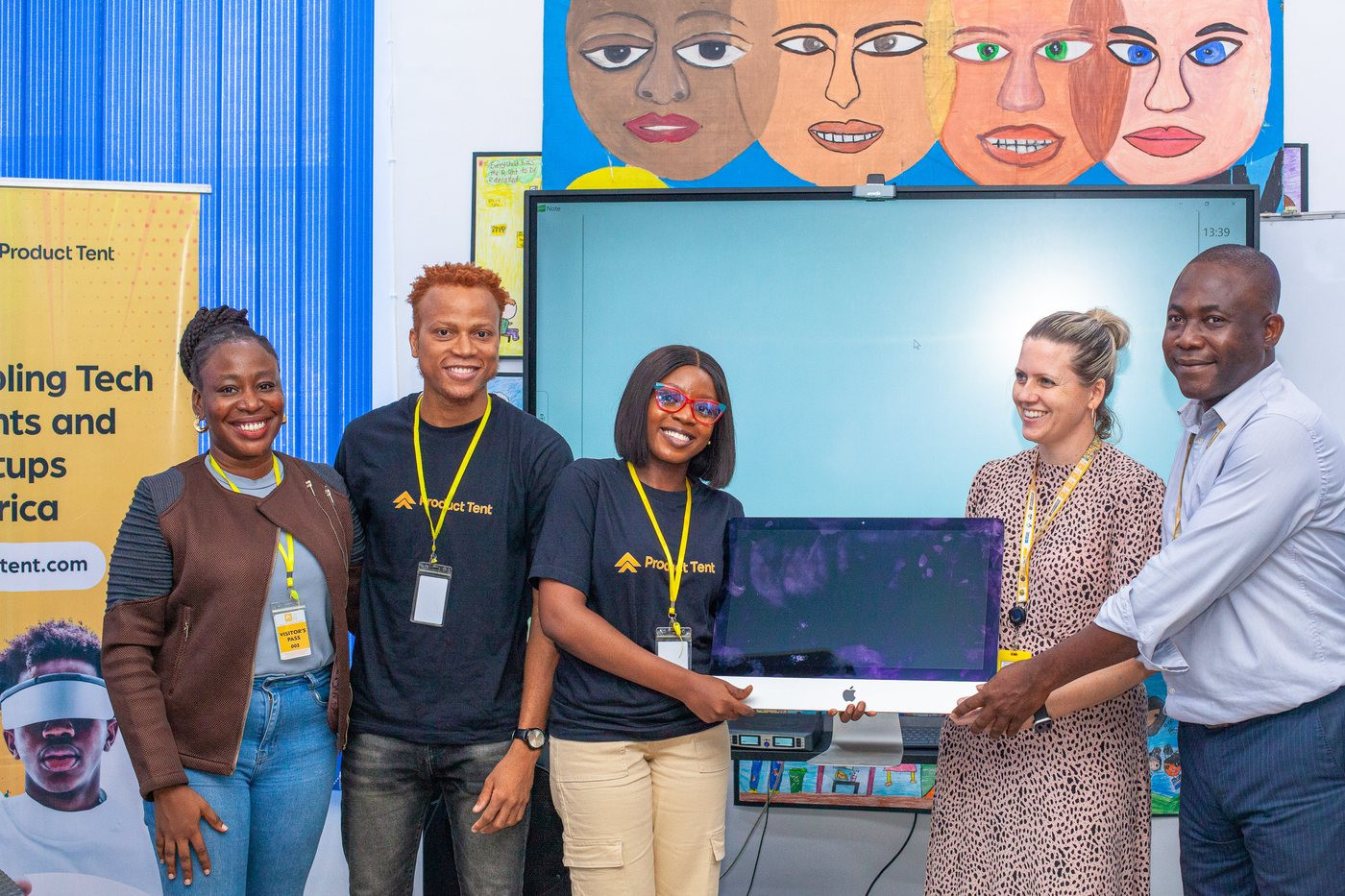 Five people standing together for a photograph at a device handover event, with a desktop computer in front of them.